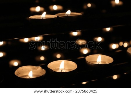Small church votive candles in a row and some others in the background at different heights lightened up inside a Catholic church during a mass