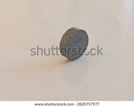 a small circular dark gray ferrite magnet balanced on edge over a light background, targeted for physics education, industrial supply catalogs, electronic engineering blogs, and science materials.