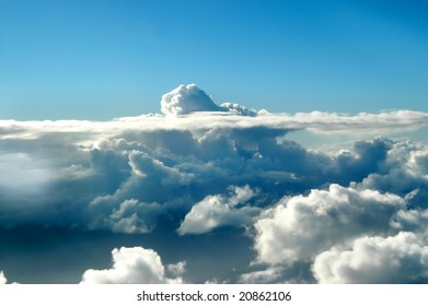 Small cloud head peaks through a layer of stratus. Blue skies.