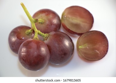 Small Cluster Of Ripe And Red/purplish Seedless Grapes Isolated On White Background. Half Cut Fruit Shows No Seeds. Berry Fruits With Stem, Flowering Plant. Close Up Photo. March 20, 2020