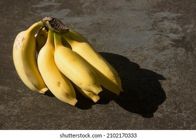 A Small Cluster Of Ripe Yellow Plantain On The Floor In Sunlight 