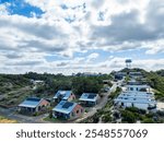 Small coastal holiday townsite with rows of various types tourist accommodation facing the beachfront, white clouds in a blue sky.