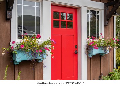 Small Colorful Wooden Garden Shed With A Red Door And Window Baskets Of Flowers.