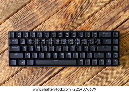 Small compact black gaming computer keyboard on a table made of wooden pine boards. Wireless keyboard with mechanical switches for gadgets and computer. Copy space. Close-up