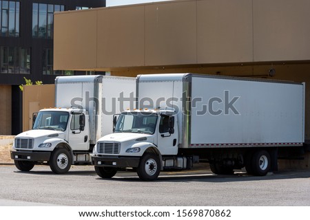 Small compact commercial industrial grade professional rigs semi trucks with long box trailers standing in warehouse dock loading different cargo for next timely delivery