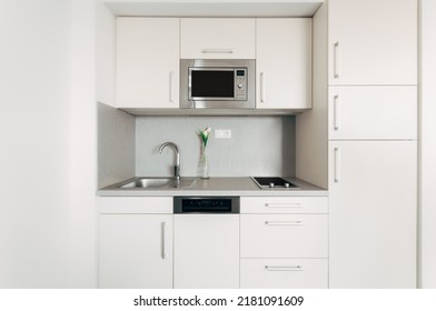 Small compact kitchen unit in modern style with several cabinets and drawers with handles. Kitchen includes built-in appliances. The line is diversified by a simple vase with several flowers. - Shutterstock ID 2181091609