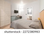 Small compact stylish bedroom in stylish soothing colors with double bed, TV, built-in wardrobe and table. Concept of small cozy bedroom or hotel room