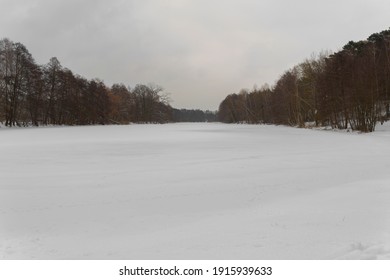 Small Completely Frozen Lake In The Village Of Gottow In Germany, Ice Sheet Covered With Snow