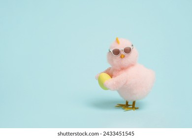 small cool chick in sunglasses with Easter egg on blue background, copy space