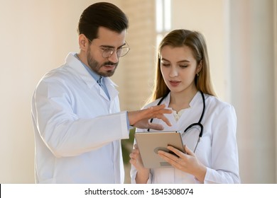 Small council of physicians. Experienced confident male doctor sharing his point of view with intern or younger female colleague using pad, discussing patient diagnosis, proposing treatment pattern - Powered by Shutterstock