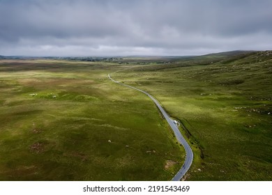 Small Country Road In A Vast Green Field By A Hill. Cloudy Sky. West Of Ireland. Irish Landscape. Empty Country Side.