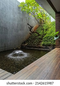 small courtyard garden with water fountain, wooden deck flooring, clear sky void with concrete rustic rough wall texture