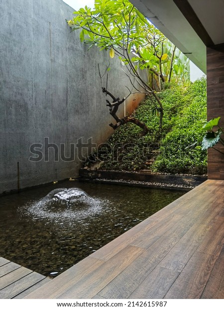 small
courtyard garden with water fountain, wooden deck flooring, clear
sky void with concrete rustic rough wall
texture