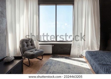 small cozy bedroom in modern apartment. bed with textile blanket, soft armchair, window with white curtains and rug on wooden laminate floor in hotel room
