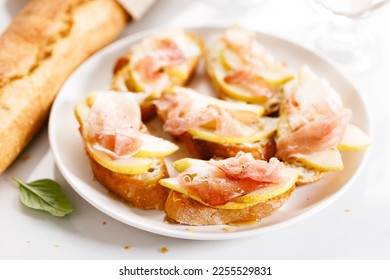 Small crostini appetizers with sliced pear and smoked ham on white plate. Closeup. - Shutterstock ID 2255529831