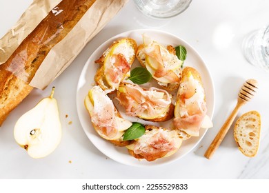 Small crostini appetizers with sliced pear and smoked ham on white plate. Closeup. - Shutterstock ID 2255529833