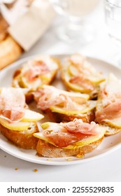 Small crostini appetizers with sliced pear and smoked ham on white plate. Closeup. - Shutterstock ID 2255529835