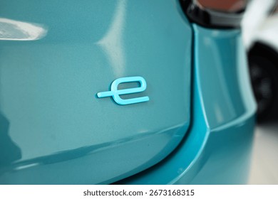 Small, cursive, type letter e, symbolizing electrification or fully electric vehicle. Close up shot, new car boot lid, no people