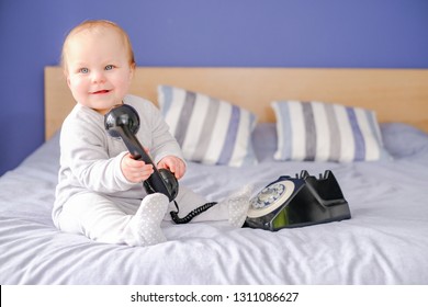 Small Cute Baby On A Comfy Bed Using An Old Fashioned Style Phone, Listening To A Phone Call Explaining Brexit.