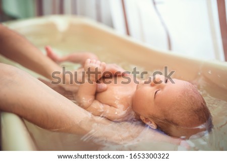 Small cute big-eyed beautiful baby bathes in warm water in the hands of a caring mother. The concept of baby care and child care