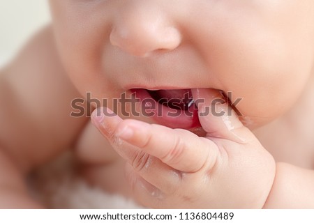 Small cute funny baby infant teething with face expression hands and fingers in mouth sore gums soothe