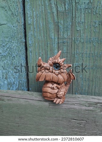 A small cute toy dragon (toy, property of the author of the photo) stands against the background of an old wooden building.