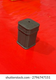 A small, dark brown, rectangular object with a textured surface and a hole on top sits on a red surface.