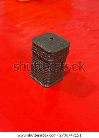 A small, dark brown, rectangular object with a textured surface and a hole on top sits on a red surface.