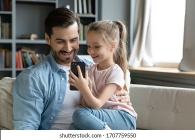 Small daughter seated on father lap showing him cool game on smartphone in internet. Parental control, protect child from forbidden content and access, new generation and mobile electronic fun concept - Powered by Shutterstock