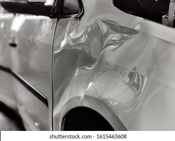 A Small Dent In The Fender Of A White Metallic European Car