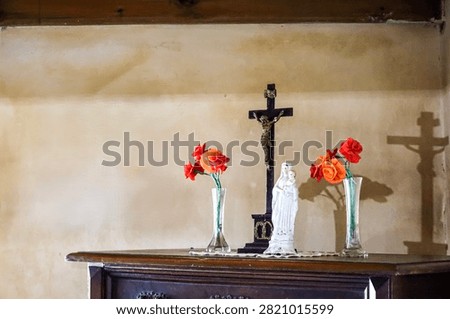 A small devotional altar featuring a crucifix, a statue of Mary holding baby Jesus, and vases of artificial roses casting shadows