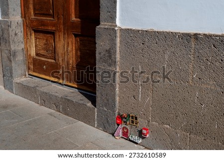 A small devotional display sits at the base of a building beside a wooden doorway.