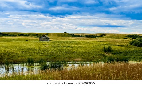 Small dilapidated shack in a large green pasture set in front of pond - Powered by Shutterstock