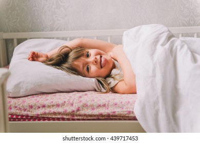A small diseased girl in the bedroom. Little girl sitting on a bed wearing a pajamas. girl is sick. girl measures the temperature. She feels bad. Sick little girl lying in the bed with thermometer
