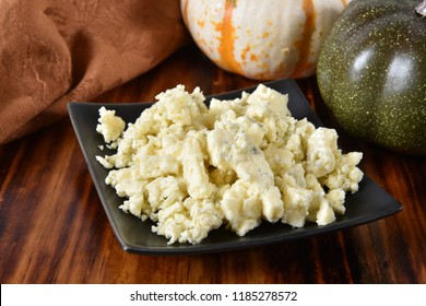 A Small Dish Of Blue Cheese Crumbles On A Cutting Board.