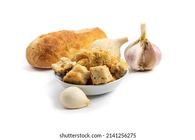 A small dish of seasoned croutons with the Italian bread the croutons are made from and several cloves of garlic isolated on white
