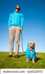 Small Dog Standing Outdoors With His Best Friend Owner In Matching Blue Hoodies On Bright Green Field