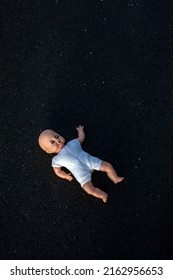 Small Doll Lying On Black Asphalt