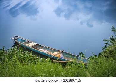 small dory boat moored to shore at a placid lake reflecting clouds and blue sky (view near)