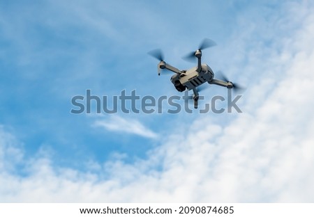 Small drone flying in a cloudy blue sky.