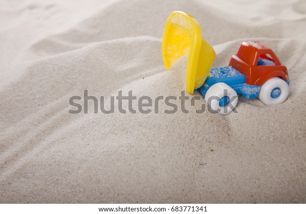 Small dump truck\
empties sand. Miniature. Children play in the sand. Sand therapy.\
Psychology and\
construction.