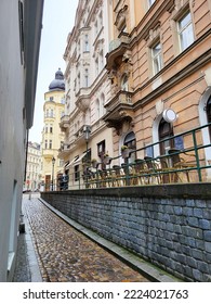 A small elevated cafe sits beside a narrow cobblestone street in old Prague.  Dynamic perspective shot of narrow back street and colourful buildings.   