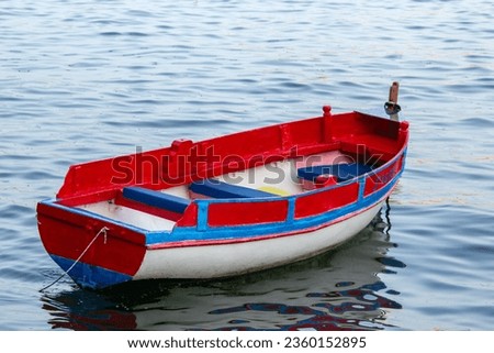 A small empty red boat on the wavy water