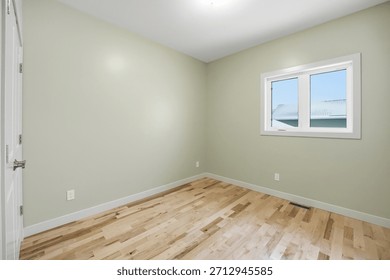 Small, empty room with a white wall and wooden floors. The room has a window that lets in natural light and a door that leads to the outside. The room is simple and uncluttered, giving it a clean