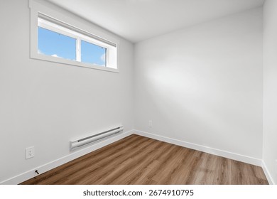 Small, empty room with a window and a radiator. The room is white and has wooden floors