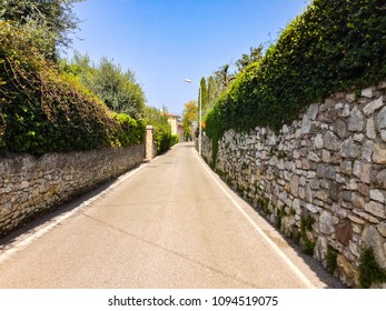A small empty street between stone fences overgrown with greenery