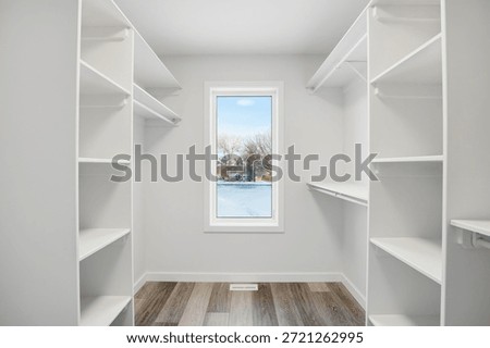 Small, empty walk in closet with a window. The window is frosted and the closet is white