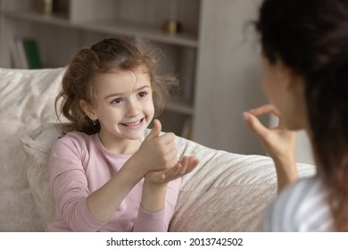 Small ethnic girl child make hand gesture talk with mom use sign language. Smiling little biracial numb deaf disabled kid communicate with tutor or coach. Disability, nonverbal communication concept. - Powered by Shutterstock