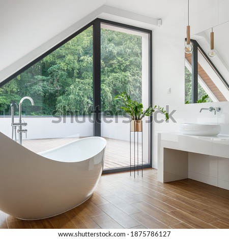 Small and exclusive attic bathroom with elegant freestanding bathtub, big window to balcony and wooden floor