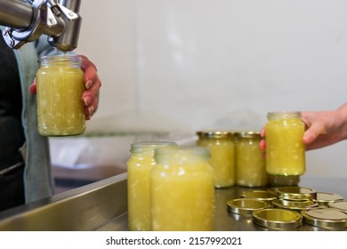 Small Family Business Food Production Company Glass Jars Of Sauce Being Filled By Hand And Screw Caps Being Placed On The Jars In There Kitchen